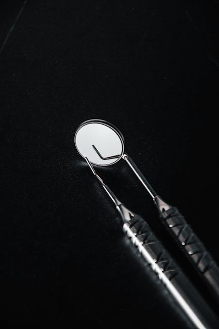 Vertical shot of dental mirror and pick tools on a black background, ideal for medical themes.
