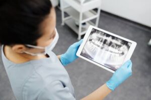 Dentist reviewing dental x-ray image on a tablet in a clinic setting, showcasing modern technology in dental care.